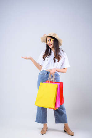A young Asian woman stand holding a multicolored shopping bag and stretched out her hand with a happy face on white background. Holiday Shopping.の写真素材