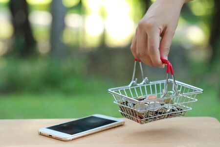 human hand holding shopping cart and coins on smart phone, idea for shopping and online payment using as business backgroundの写真素材