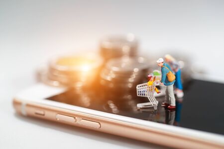 Miniature people: shopper standing on cell phone with money beside idea for payment and purchase online (e-commerce and shopping concept)の写真素材