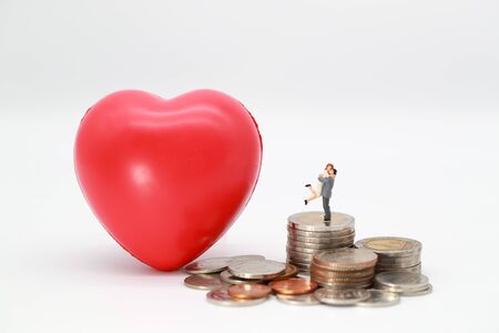 Miniature people: a couple standing on stacking coin with read heart symbol , idea for saving money for loveの写真素材