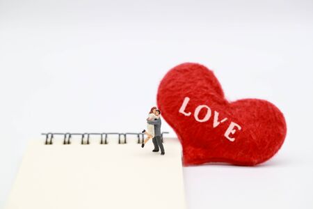 Miniature people: a couple standing on notebook with read heart symbol, idea for valentine backgroundの写真素材