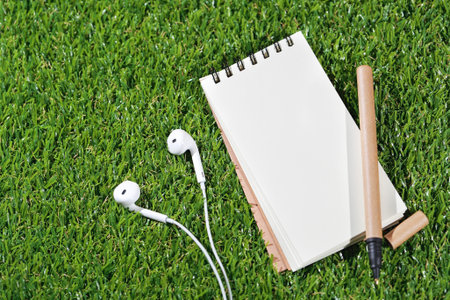 notebook and pen on top with earphone on grass (travel concept)