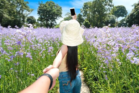portrait of a couple holding hand among Naga flower crested field in nature while woman using cell phone take themselves photoの写真素材