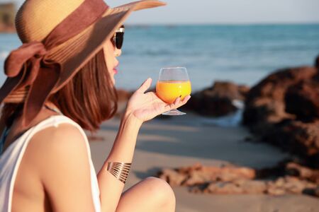 portrait of beautiful and happiness woman enjoy holiday vacation with orange juice on the beachの写真素材