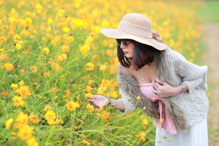 cute and beautiful girl with hat standing in nature outdoors among cosmos flowers field (rest time on vacation concept)の写真素材