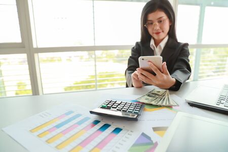 businesswoman using cell phone and computer while working on  company summary report with graphの写真素材