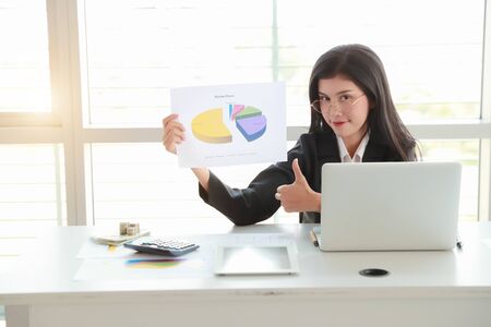 businesswoman showing thumb up and company profit with graph in meeting roomの写真素材