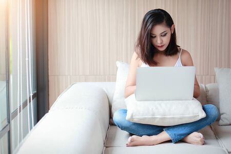 beautyful woman portrait using computer with white vest and blue jean in living room on relax dayの写真素材