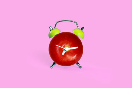 apple in alarm clock on pink pastel desk