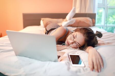 beautiful and sexy woman using laptop computer and listening to music from cell phone on bedの写真素材