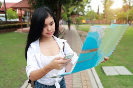 Young asian traveler using cell phone and holding map in temple while traveling during holiday vacationの写真素材