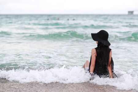 back view portrait of fashion and sexy girl with black hat on the beach and blue skyの写真素材
