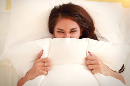 portrait of beautyful model with black see through dress closing her mouth with pillowsの写真素材