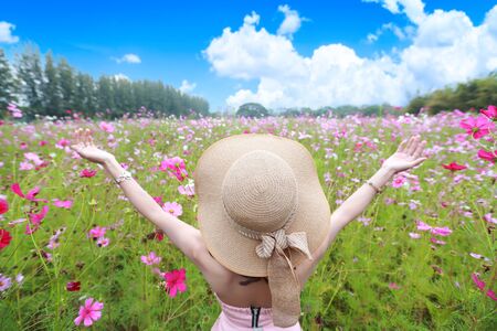 cute and beautiful girl with hat standing in nature outdoors among cosmos flowers field (rest time on vacation concept)の写真素材