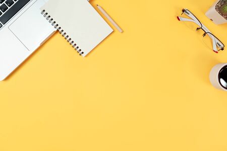 workspace business desk with computer, coffee cup, notebook and glasses on yellow pastel backgroundの写真素材