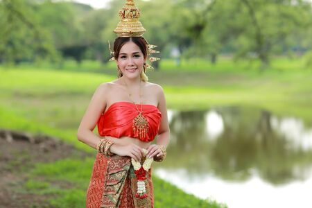 fashion asian girl in Thai traditional costume in ancient temple with steering wheel flower in handの写真素材