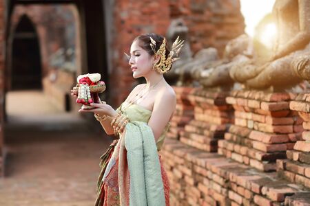 fashion asian girl in Thai traditional costume in ancient temple with steering wheel flower in handの写真素材