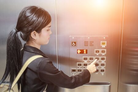 businesswomen pressing elevator button with sun light effect.の写真素材