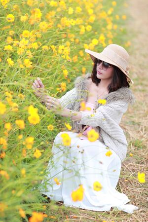 cute and beautiful girl with hat standing in nature outdoors among cosmos flowers field (rest time on vacation concept)の写真素材