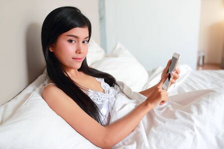 young and sexy woman using cell phone on bedの写真素材