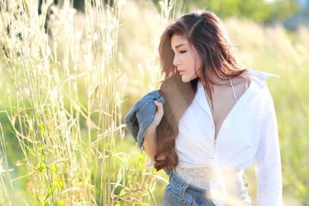 portrait of beautiful woman wearing white shirt and blue jean having a happy time and enjoying among grass field in natureの写真素材