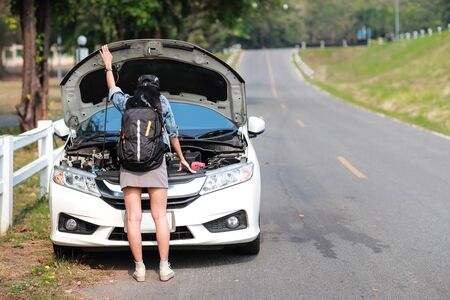 Young asian traveler women with backpack got car broken and waiting for helpの写真素材