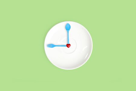 wall clock with blank dish, heart symbol, fork and spoon on green pastel backgroundの写真素材