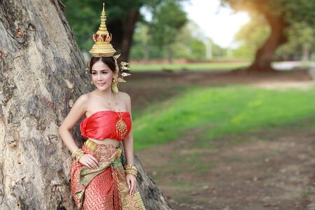 young fashion asian girl in Thai traditional costume standing with big green treesの写真素材