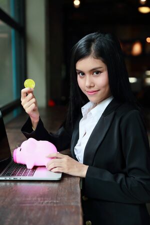 portrait of businesswoman showing bitcoin or coin on pink piggy with computer meaning of profit investment or money savingの写真素材