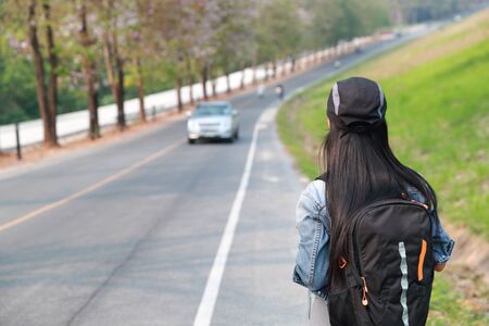 Young asian traveler with backpack waiting for car on the road while traveling during holiday vacationの写真素材