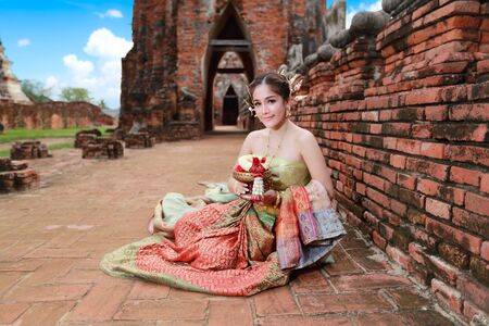 fashion asian girl in Thai traditional costume in ancient temple with steering wheel flower in handの写真素材
