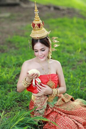 fashion asian girl in Thai traditional costume in ancient temple with steering wheel flower in handの写真素材