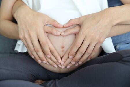 pregnant woman and husband hands doing heart symbol on their belly with loveの写真素材