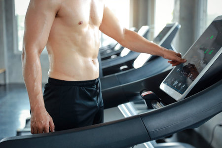image of healthy and sexy caucasian muscle man in shirtless who setting up running machine in gym
