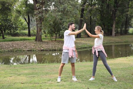young and healthy couple people enjoying in exercising outdoor and they posting give me five with green trees during summer time in the parkの写真素材