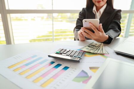 businesswoman using cell phone and computer while working on  company summary report with graphの写真素材
