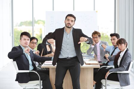 caucasian boss businessman showing thumb down or dislike with unhappy face with unsuccess multiethnic business team and business graph backgroundの写真素材