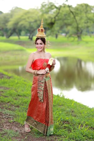 fashion asian girl in Thai traditional costume in ancient temple with steering wheel flower in handの写真素材