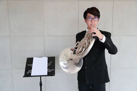 young musician man wearing black suit playing french hornsの写真素材