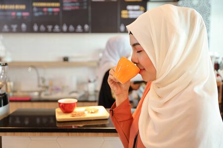 muslim customer drinking coffee at counter with young muslim barista girl working blurred backgroundの写真素材