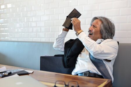 senior businessman wearing black suit viewing empty wallet because of failure from doing businessの写真素材
