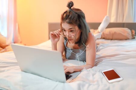 beautiful and sexy woman using laptop computer and listening to music from cell phone on bedの写真素材