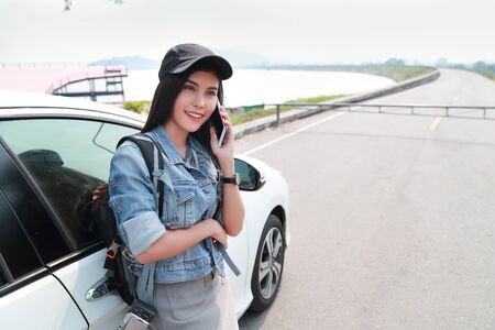 Young asian traveler with car using smart phone while traveling during holiday vacationの写真素材