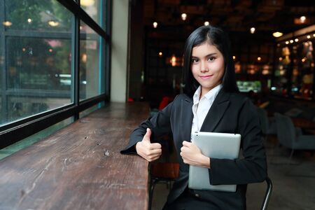 businesswoman showing thumb up and victory symbol on her hands for meaning success project with bank notes and computer on tableの写真素材