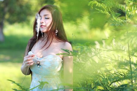 cute and beautiful girl standing in nature outdoors and holding grass flowers on her handの写真素材
