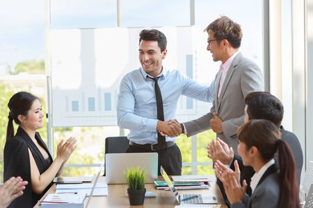 caucasian businessman showing success business profit graph from white board in meeting then they shaking their hands meaning of their job is success with smiling and happy faces.の写真素材