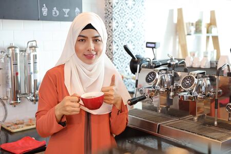 young muslim barista girl making coffee and show thumb up meaning of business successの写真素材