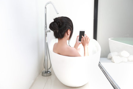 portrait of beautiful and sexy woman using cell phone while taking shower in bathtub