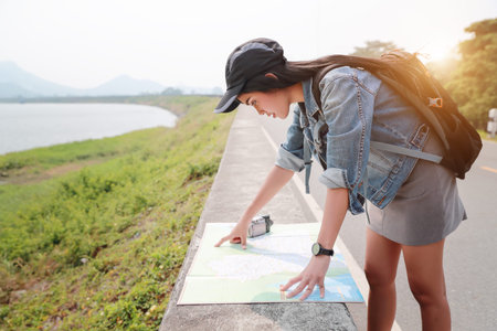 Young asian traveler searching direction on location map while traveling during holiday vacation