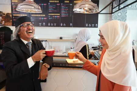 muslim customer businessman wearing black suit drinking coffee at counter with young muslim barista businesswoman backgroundの写真素材